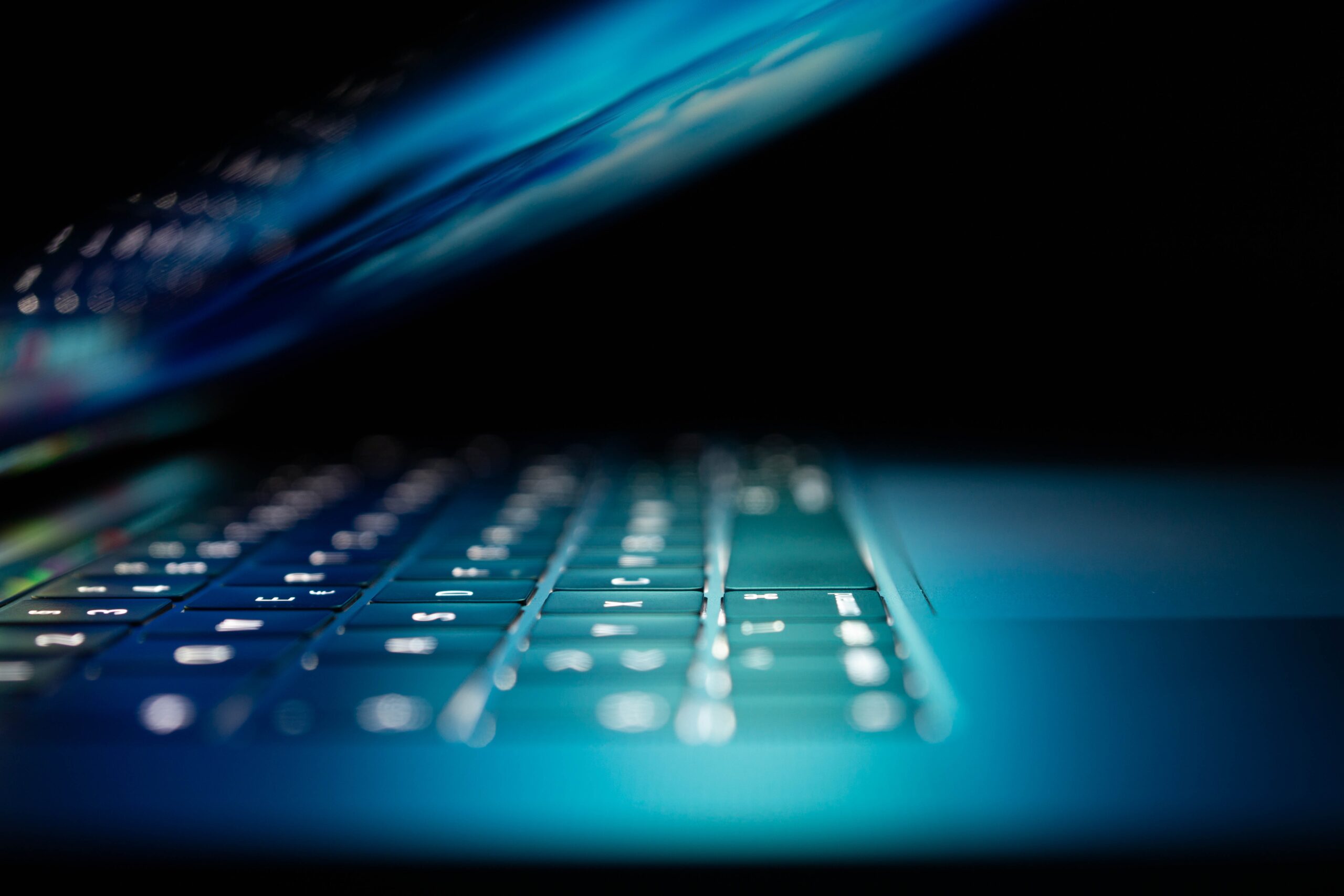 Close-up shot of a laptop keyboard with glowing blue light reflecting off the keys