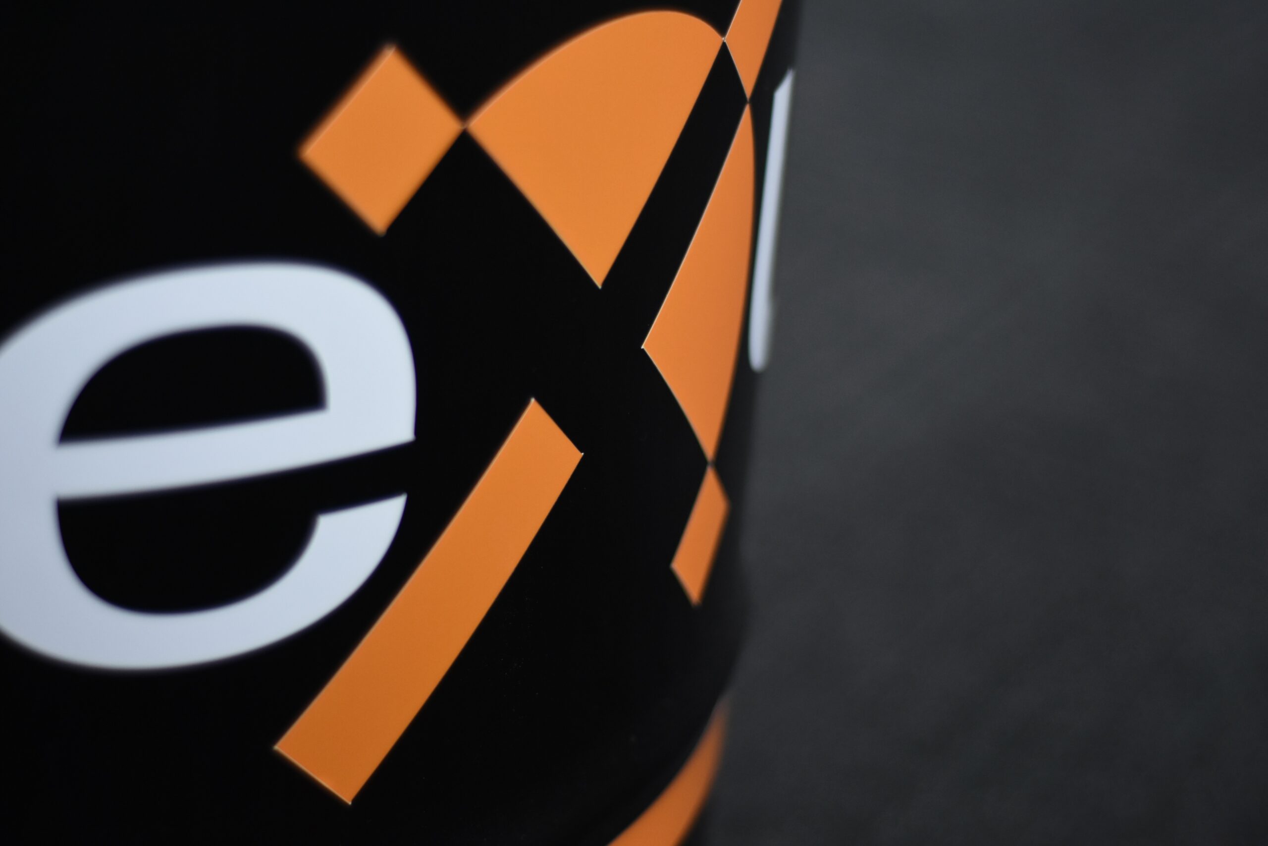 Close-up of the Nexus logo showing a bold orange and black geometric design with the letter “e” in white