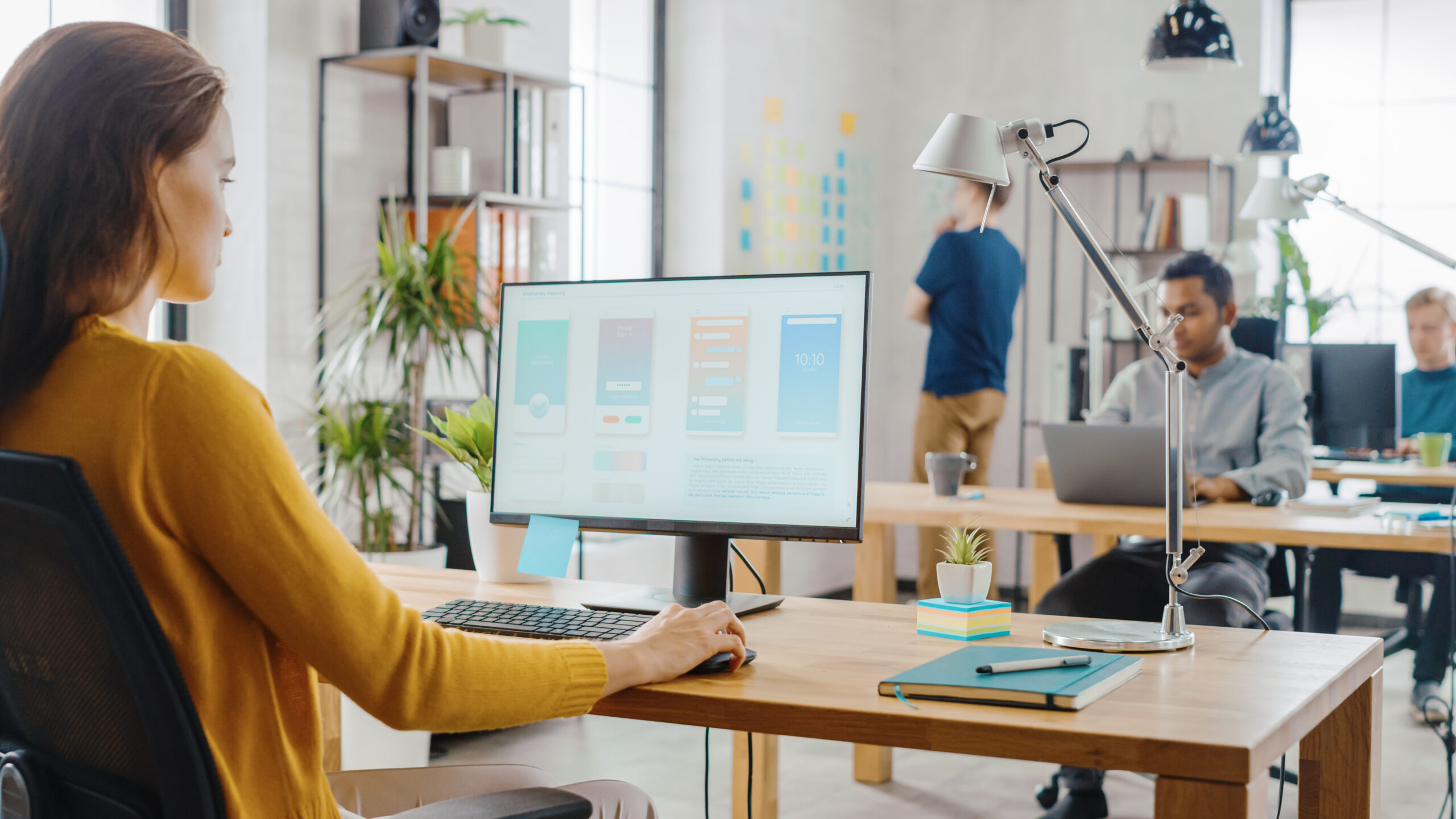 Woman Sitting at Her Desk Using Desktop Computer with Screen Showing Project Management
