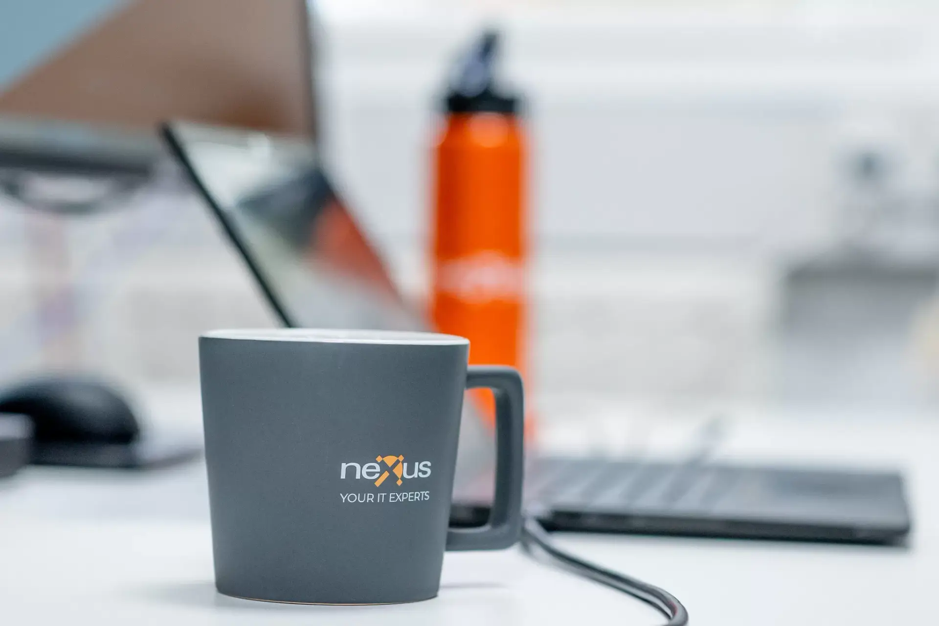 Nexus branded coffee mug on office desk with blurred laptop and water bottle in the background
