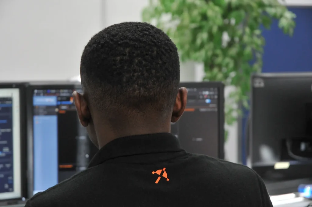 Back view of a Nexus IT Experts employee in branded polo shirt, working on multiple monitors