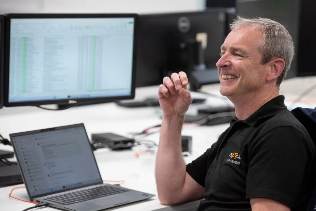 Staff member in branded polo shirt laughing during a team conversation at his workstation