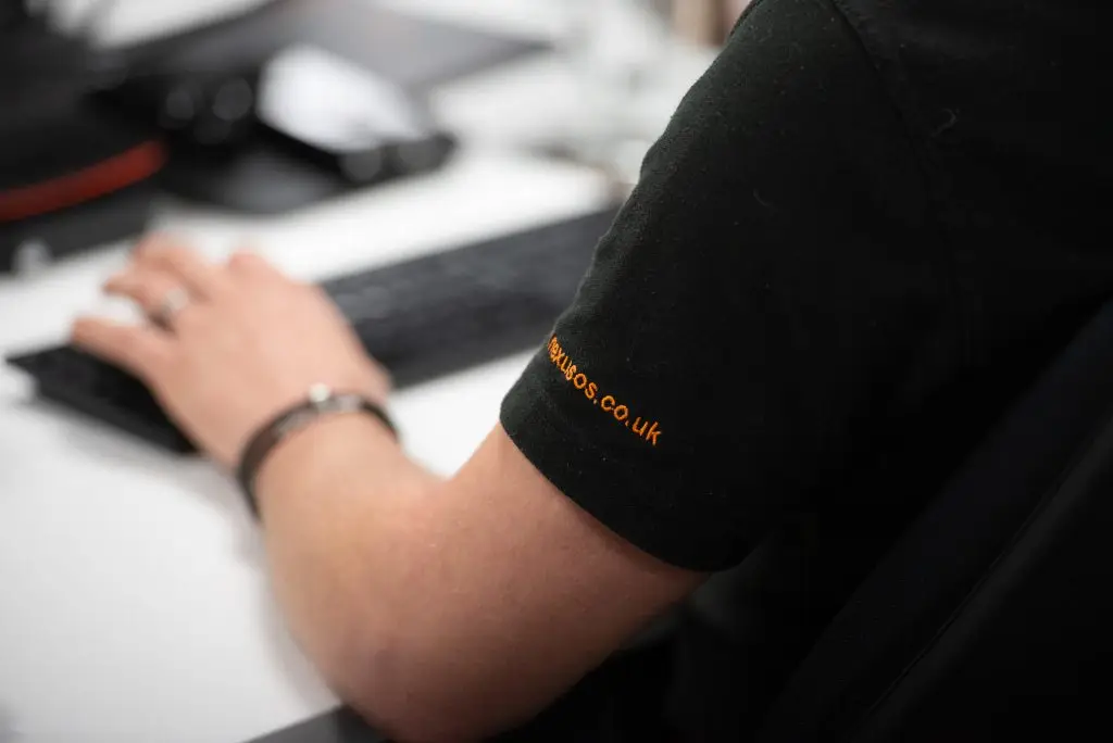 Close-up of a Nexus Open Systems team member typing at a keyboard, wearing a branded polo shirt in an office setting