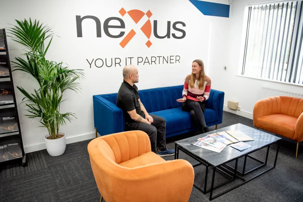Two colleagues having a discussion in the Nexus office reception with company branding on the wall