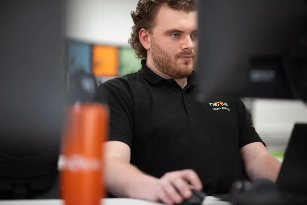 Nexus Open Systems engineer focused at his workstation, providing IT support and monitoring systems on dual screens.