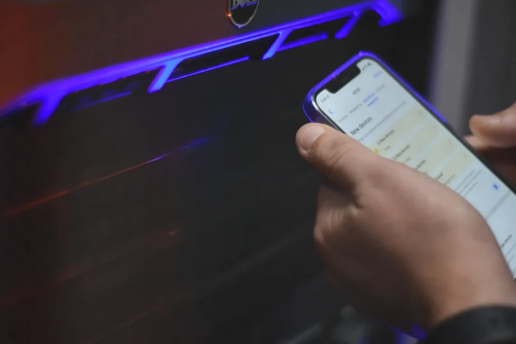 Close-up of Nexus IT Experts employee holding a smartphone while configuring device settings near a computer setup with neon light