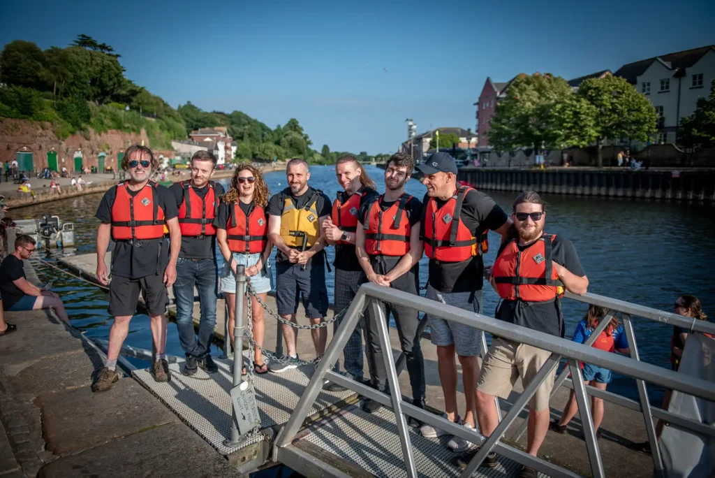 Nexus IT Experts team members wearing life jackets, smiling together on a riverside dock during a company outing
