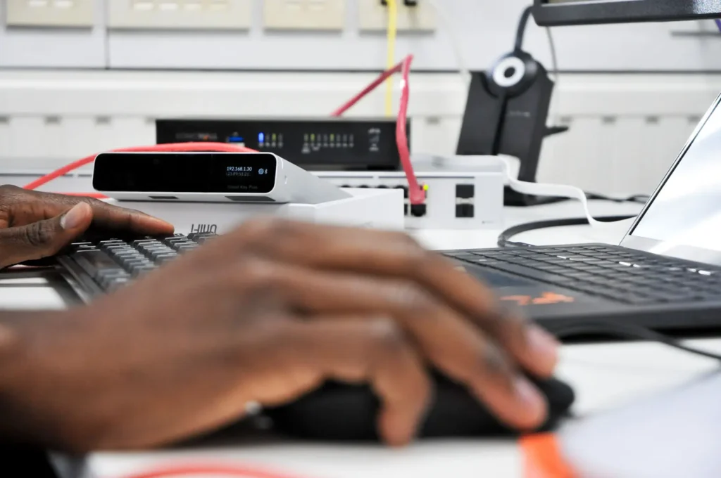 Close-up of hands on a keyboard with Nexus networking hardware and router in the background