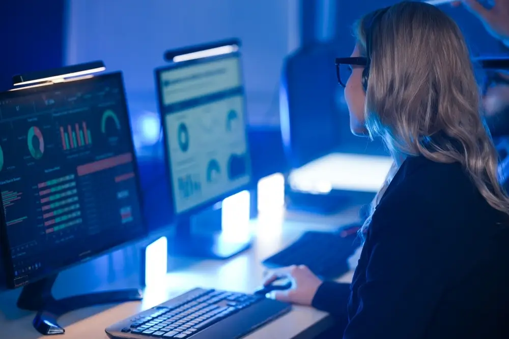 Person analysing data dashboards on dual monitors in a modern office setting